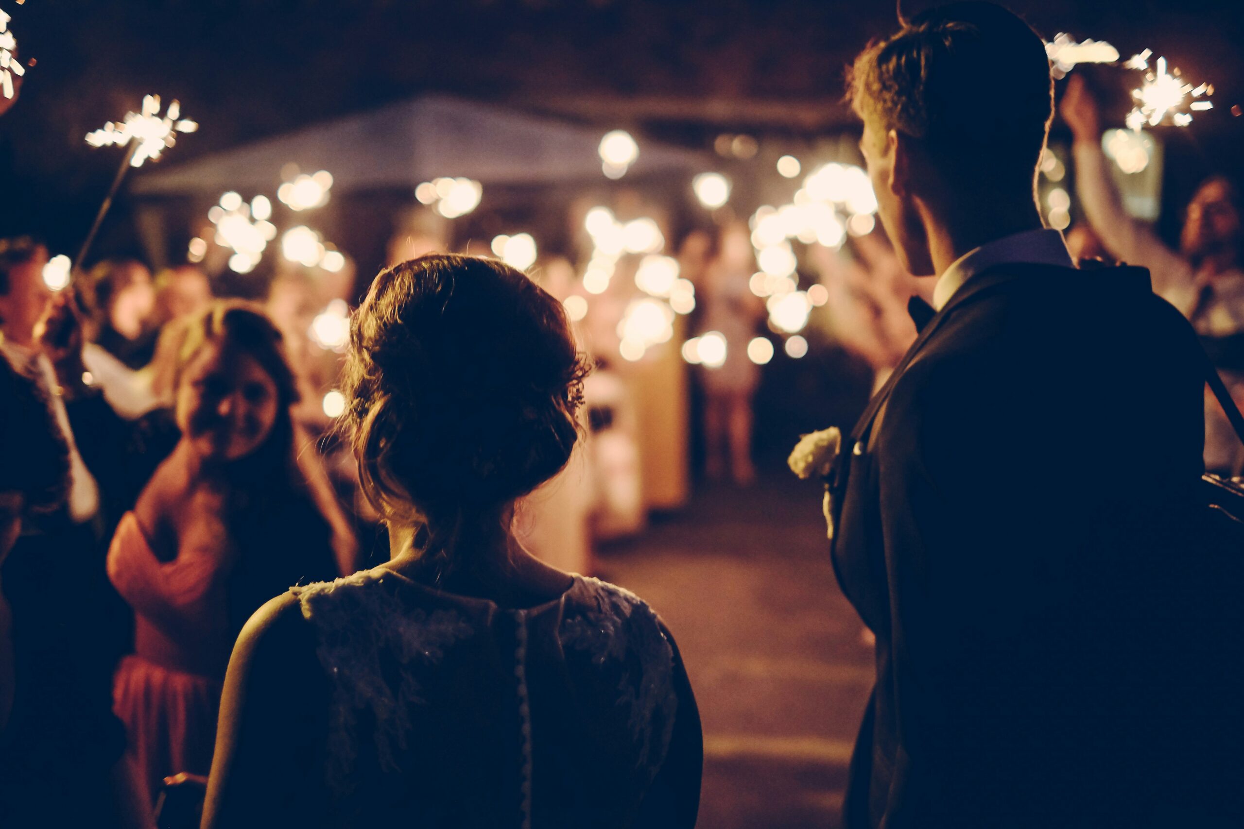 Dark image of a wedding party waving sparklings at night for couple