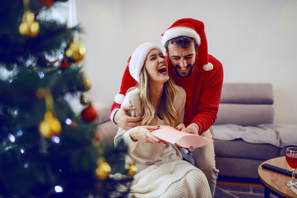 Female and male in Santa hats laughing with Christmas tree in the foreground