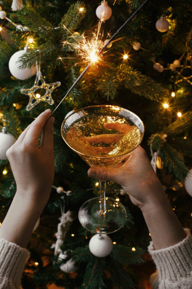 Woman holding cocktail and sparkler in front of Christmas tree