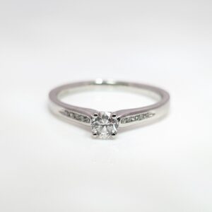 A classic four claw 0.30ct solitaire diamond engagement ring with diamond set shoulders, in a sleek platinum band.